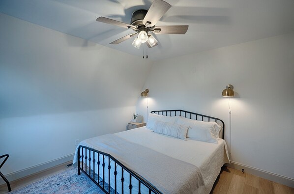 Un dormitorio con cama, ventilador de techo, dos lámparas de pared y una alfombra estampada.