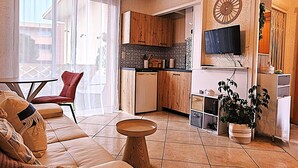 A modern living room with a sofa, a small table, and a kitchen area with wooden cabinets and a TV. - Modern 30m² Apartment with A/C & Wi-Fi – Just 100m from the Beach (Fréjus)