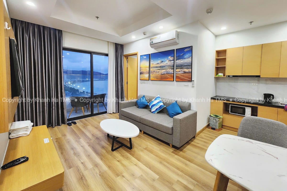 A modern living room with a grey sofa, a white coffee table, and a view of the city through large windows.