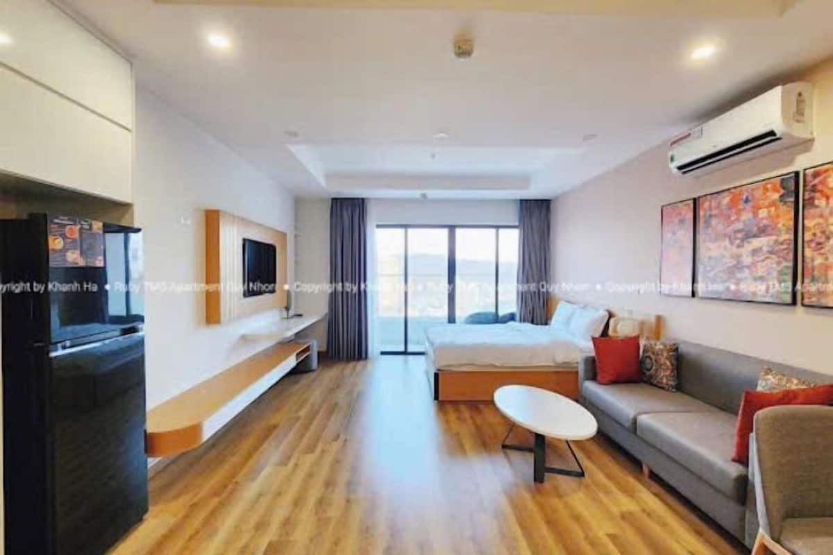 A modern hotel room with a bed, sofa, TV, and artwork.