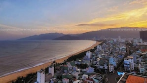 A coastal cityscape with a beach and buildings along the shore. - TMS QUY NHON- RUBY LUXURY SEA APARTMENT (Quy Nhon)