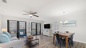 A spacious living area with a sofa, coffee table, and dining table with chairs. There is a ceiling fan, a TV, and artwork on the wall. - NEWLY RENOVATED 2BR 2BA CONDO - FREE BEACH SERVICE (Destin)