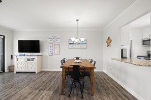 A dining area with a wooden table and chairs, a TV on a cabinet, and artwork on the walls. - NEWLY RENOVATED 2BR 2BA CONDO - FREE BEACH SERVICE (Destin)