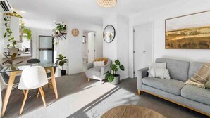 Una sala de estar moderna con un sofá gris, una mesa de comedor con sillas y una zona de cocina con plantas y un reloj en la pared.