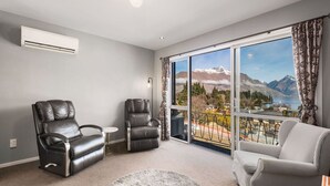A room with two leather chairs, a small round table, and a large window with a view of mountains and a lake. - Balla-Rama Stunning Views - Town Center - Parking (Queenstown)