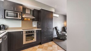 A modern kitchen with dark cabinetry, a microwave, a stove, and a built-in oven. There are two black leather chairs and a small table in the adjacent area. - Balla-Rama Stunning Views - Town Center - Parking (Queenstown)