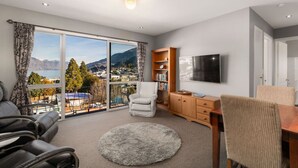 A spacious living room with a large window offering a scenic view, a comfortable sofa, a television, and a wooden cabinet. - Balla-Rama Stunning Views - Town Center - Parking (Queenstown)