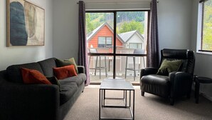A living room with a sofa, armchair, and coffee table, large windows with a view of a house and trees. - Robins Retreat-Town Center - Parking - Easy access (Queenstown)