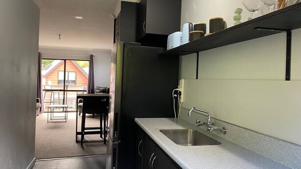 A modern kitchen with a granite countertop, stainless steel sink, and black cabinets. - Robins Retreat-Town Center - Parking - Easy access (Queenstown)