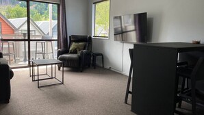 A modern living room with a large window, a flat-screen TV, and a small table. - Robins Retreat-Town Center - Parking - Easy access (Queenstown)