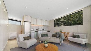 Sala de estar moderna com um sofá cinza, uma mesa de centro redonda de madeira e uma grande janela com vista para uma floresta.