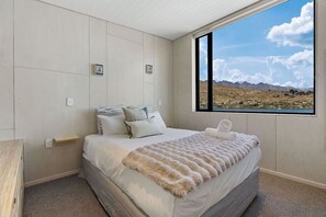 Ein Schlafzimmer mit einem großen Fenster, einem Bett mit weißer Bettwäsche und Blick auf Berge.