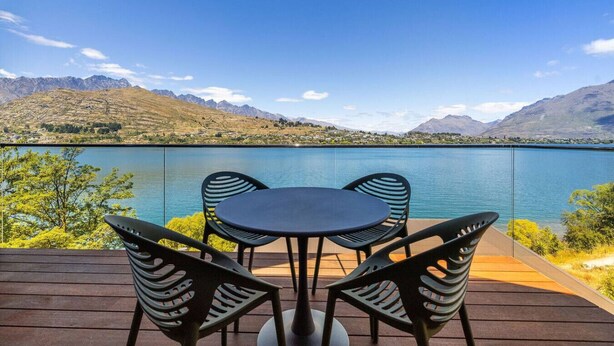 Um terraço com mesa e cadeiras, com vista para um lago e montanhas ao fundo.