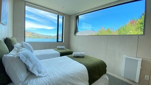 Quarto de hotel com duas camas, uma janela grande e vista para as montanhas, e um radiador.