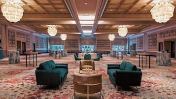 Eine geräumige Lobby mit Teppichmuster, grünen Sofas, einem runden Tisch in der Mitte und großen Kronleuchtern.