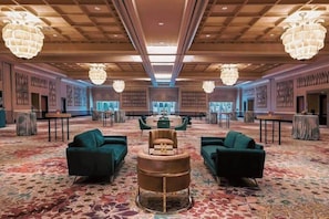 Een ruime lobby met een patroonrijk tapijt, groene banken, een ronde centrale tafel en grote kroonluchters.