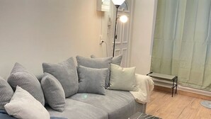 Ett modernt vardagsrum med en grå soffa, flera kuddar, en golvlampa och en bänk vid fönstret.
