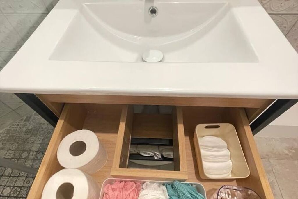 A bathroom with a white sink, a wooden vanity, and a drawer containing toilet paper, towels, and a soap dish.