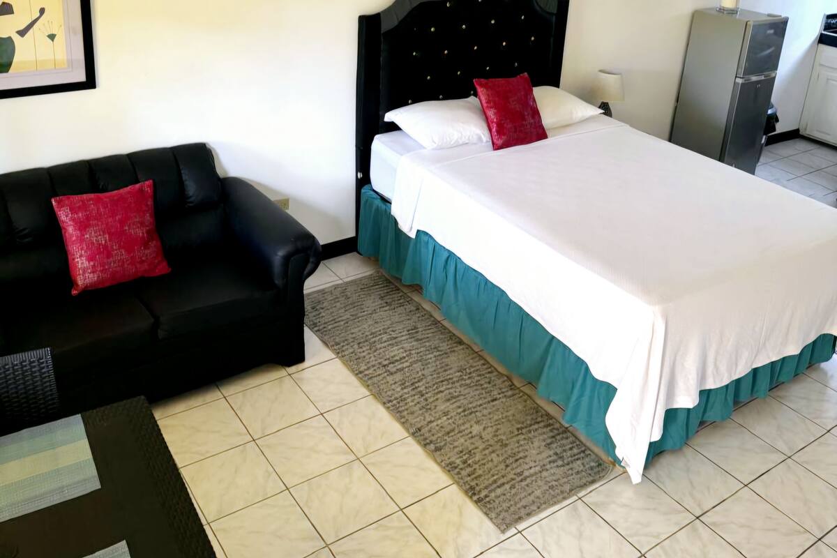 Habitación de hotel con cama, sofá negro, una mesita y un cuadro enmarcado en la pared.
