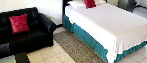 A hotel room with a bed, a black sofa, a small table, and a framed picture on the wall.