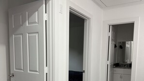 A hallway with a white door, a dark-colored room, and a bathroom with a sink and mirror. - Modern luxe townhome
-15 minutes away from downtown (Houston)