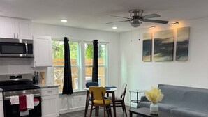 A modern kitchen with white cabinets, a microwave, and a stove. There is a dining area with a table and chairs, and a gray sofa in the living room. - Modern luxe townhome
-15 minutes away from downtown (Houston)