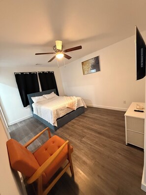 Ein Schlafzimmer mit Bett, Deckenventilator, Fernseher, Sessel und Nachttisch.