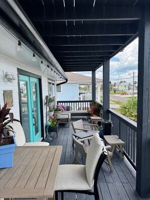 A covered outdoor seating area with tables and chairs, potted plants, and a view of the street.