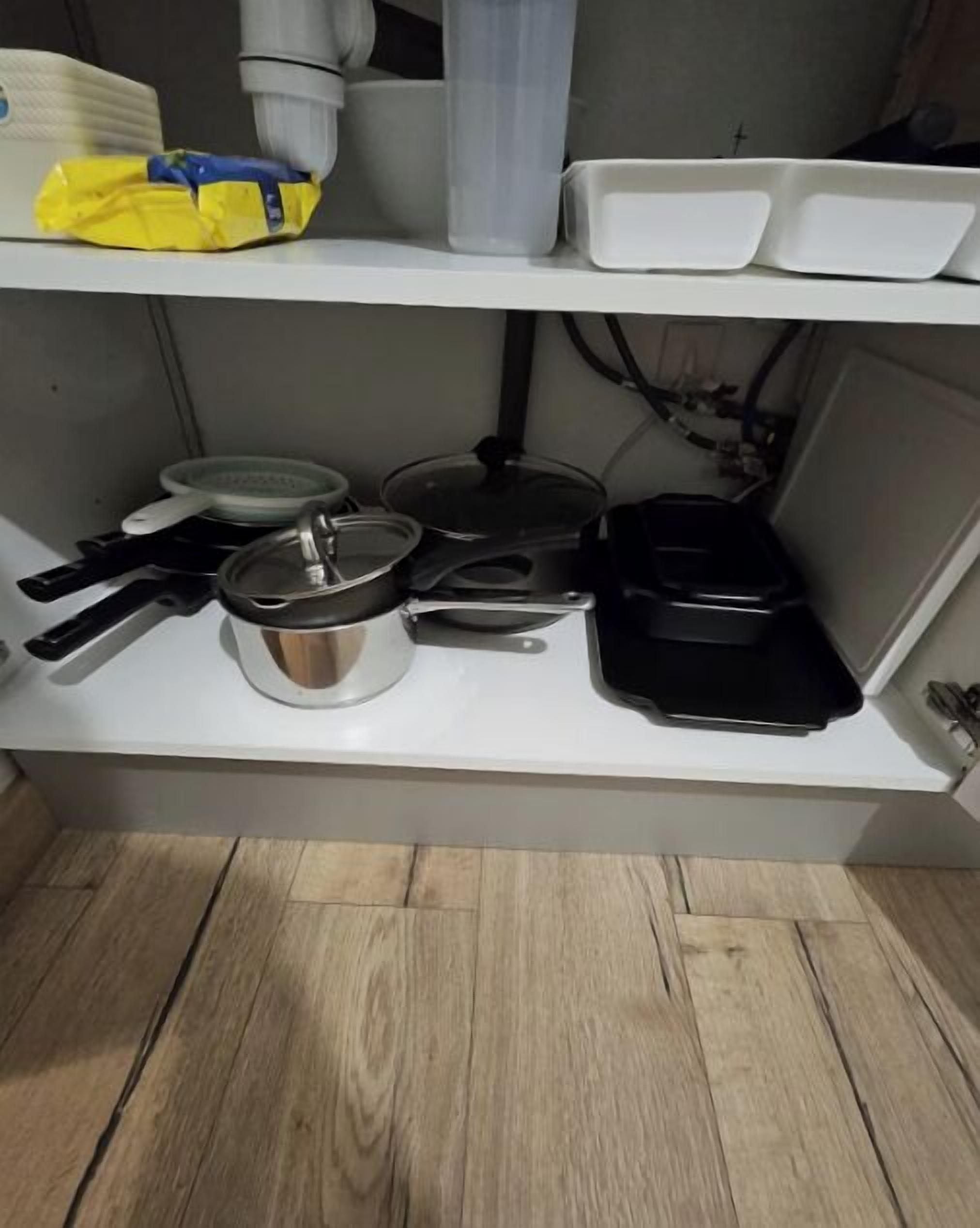 Une cuisine avec un plan de travail blanc, une casserole, une poêle et une autre poêle noire.