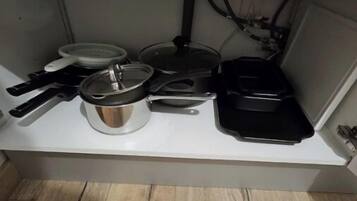 Une cuisine avec un plan de travail blanc, une casserole, une poêle et une autre poêle noire.