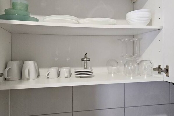 A kitchen shelf with white plates, green and white cups, and clear glasses.