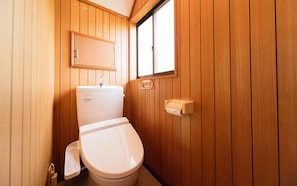 Et lille badeværelse med træpaneler, toilet, håndvask og et vindue.