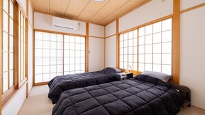 Une pièce de style japonais traditionnel, avec un sol recouvert de tatamis, deux lits dotés de draps sombres et de grandes fenêtres à cadre en bois.
