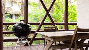 Une table et des chaises en bois sur une terrasse, avec un barbecue noir et un récipient en métal.
