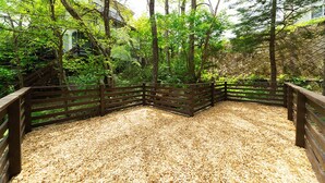 Une terrasse en bois recouverte de gravier, entourée d’arbres et d’une clôture.