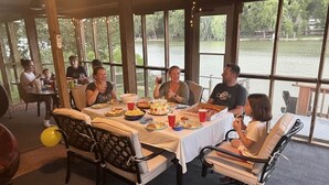 A group of people dining at a table with a view of a lake, surrounded by large windows. - Rivers Edge Retreat (Front Royal)
