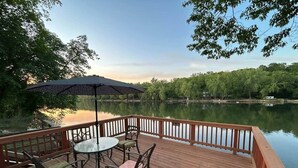 A wooden deck with a table and chairs, overlooking a calm lake with trees in the background. - Rivers Edge Retreat (Front Royal)