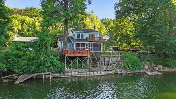 A house with a dock extending into a lake, surrounded by dense greenery. - Rivers Edge Retreat (Front Royal)