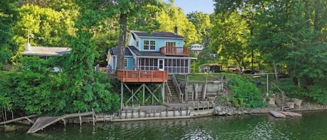 A house with a dock extending into a lake, surrounded by dense greenery.