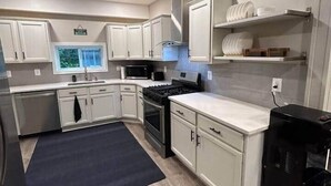 A modern kitchen with white cabinets, a black countertop, a stainless steel stove, and a black trash can. - Rivers Edge Retreat (Front Royal)