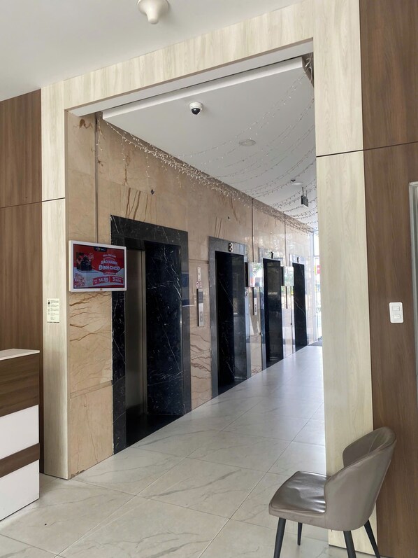A hotel lobby with marble flooring, a reception desk, and a waiting area with a chair.
