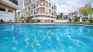 Une piscine entourée de bâtiments modernes dotés de balcons, sous un ciel dégagé, avec quelques arbres.