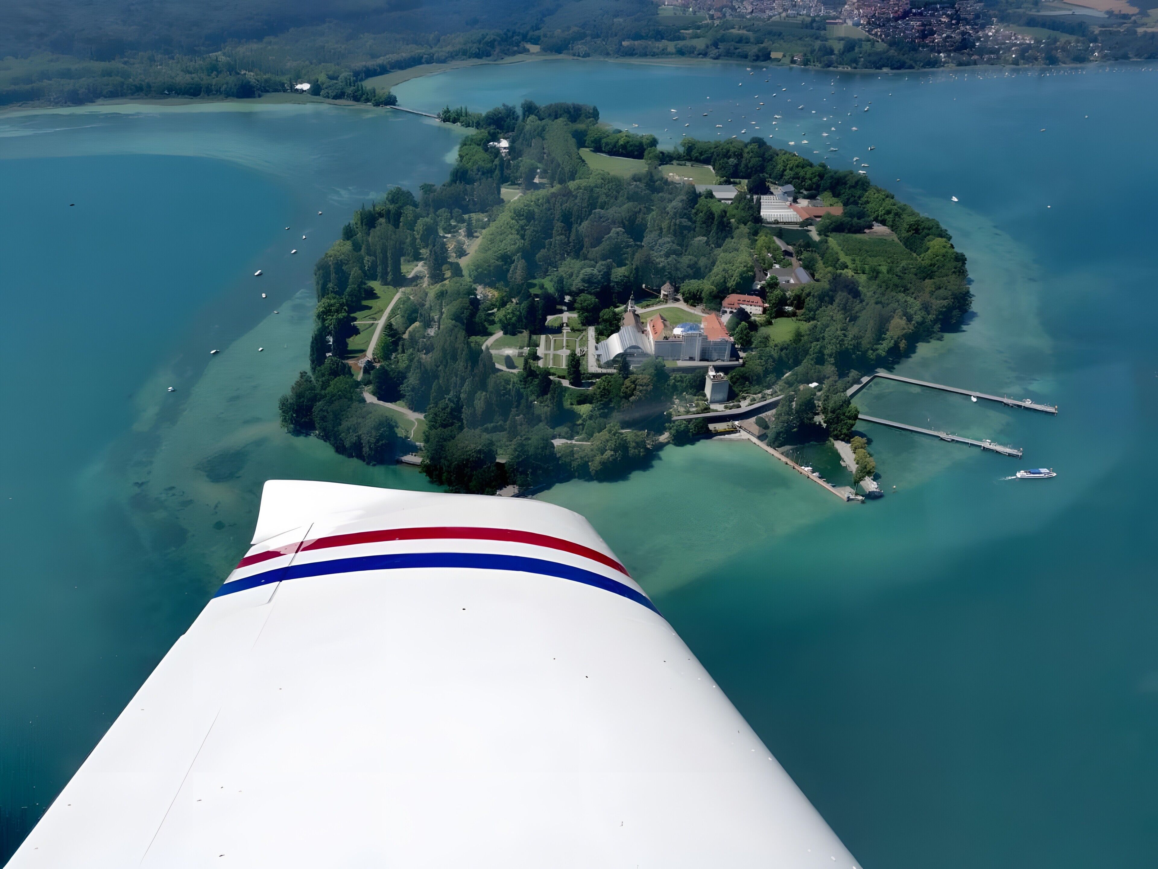 Vue aérienne d’une île avec un quai, des bâtiments et un lac d’un bleu limpide.