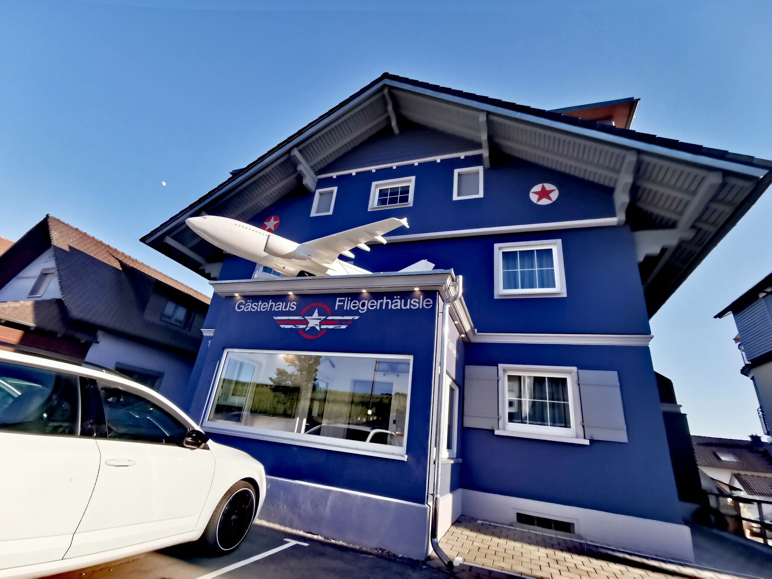 A building with a sign reading 'Gastehaus Fliegerhäuse' and a model airplane on the roof.