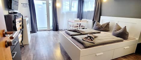 A modern bedroom with a bed, a TV, a desk, and a chair.