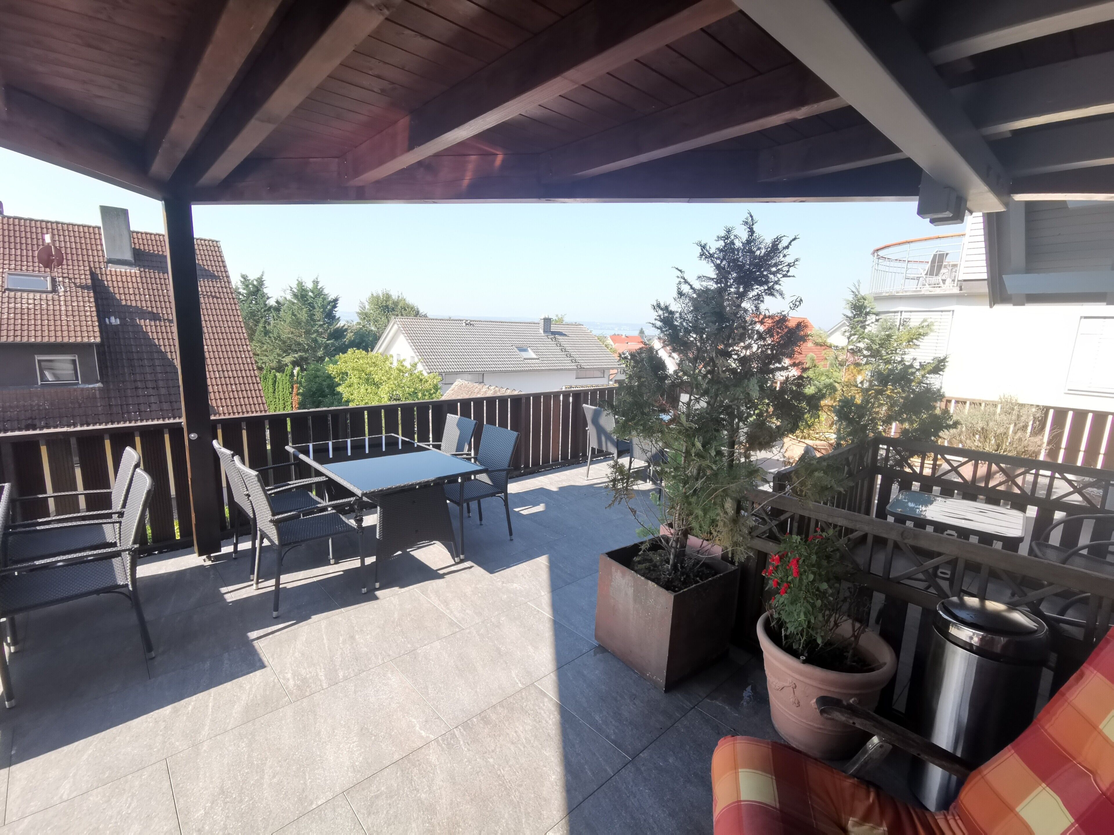 A covered patio with a table and chairs, potted plants, and a trash can.