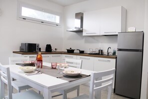 A modern kitchen with white cabinetry, a stainless steel refrigerator, and a dining table set for four.
