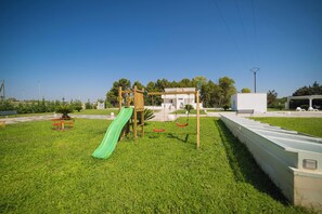 Ein Spielplatz mit einer grünen Rutsche, Schaukeln und einem kleinen Gebäude.