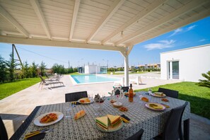 An outdoor dining area with a pool in the background.