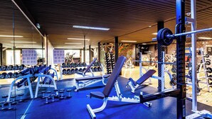 Un gimnasio con equipo de levantamiento de pesas, bancos y mancuernas.